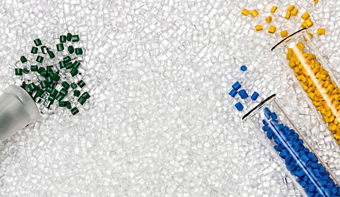 Vials filled with dyed plastic granules spilling out onto a large bed of transparent plastic granules yet to be dyed.