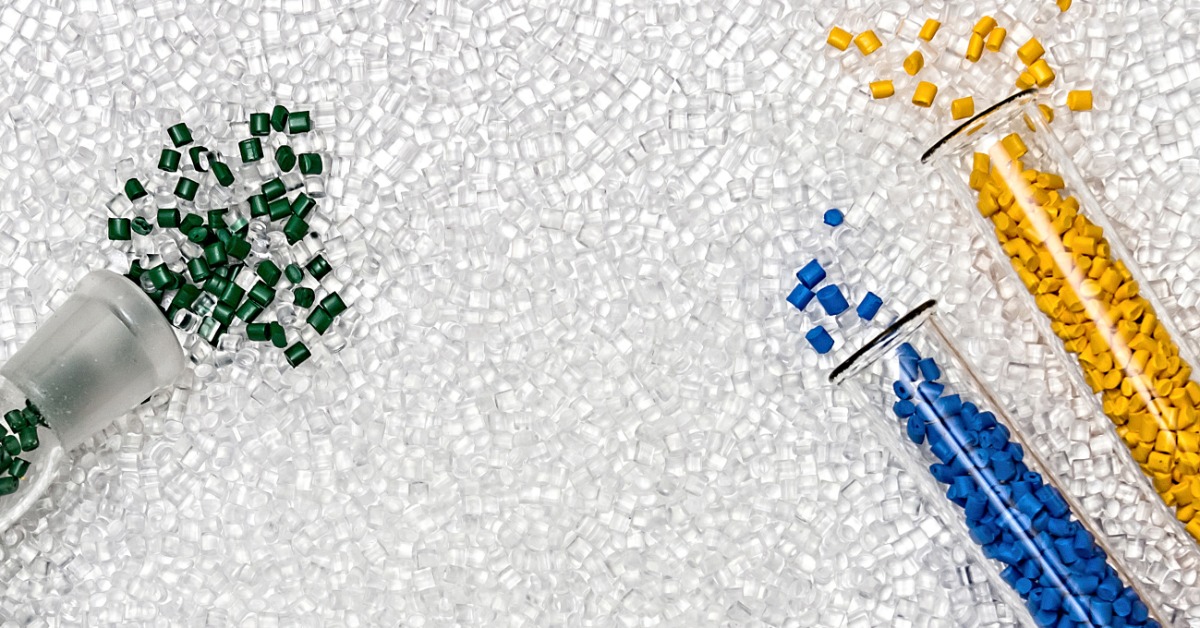 Vials filled with dyed plastic granules spilling out onto a large bed of transparent plastic granules yet to be dyed.