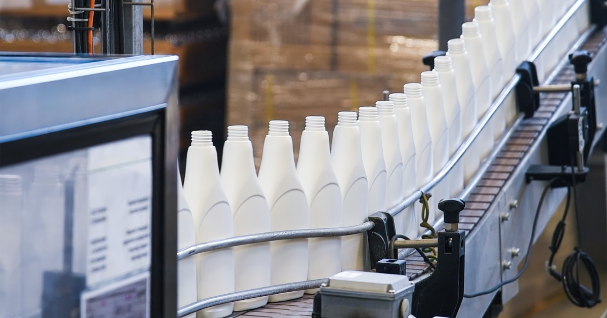 A row of white plastic bottles moving along a fully automated conveyor belt during the manufacturing process.